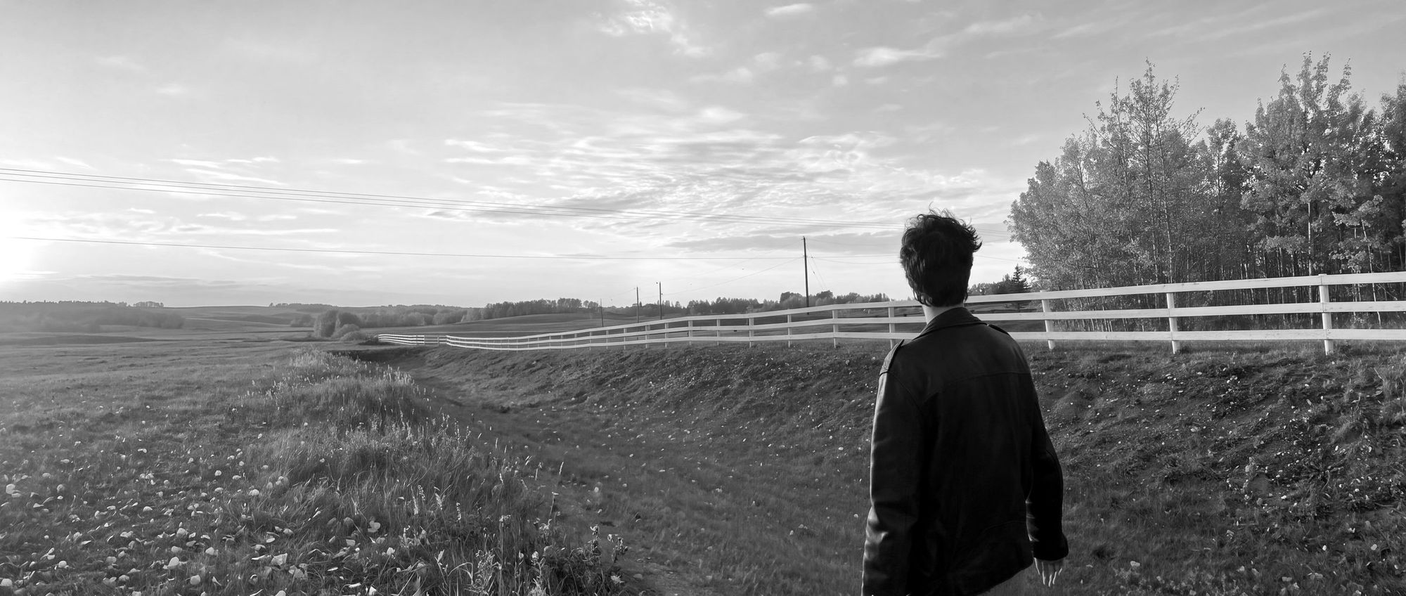 Blake walking beside a long white rail fence on the prairie